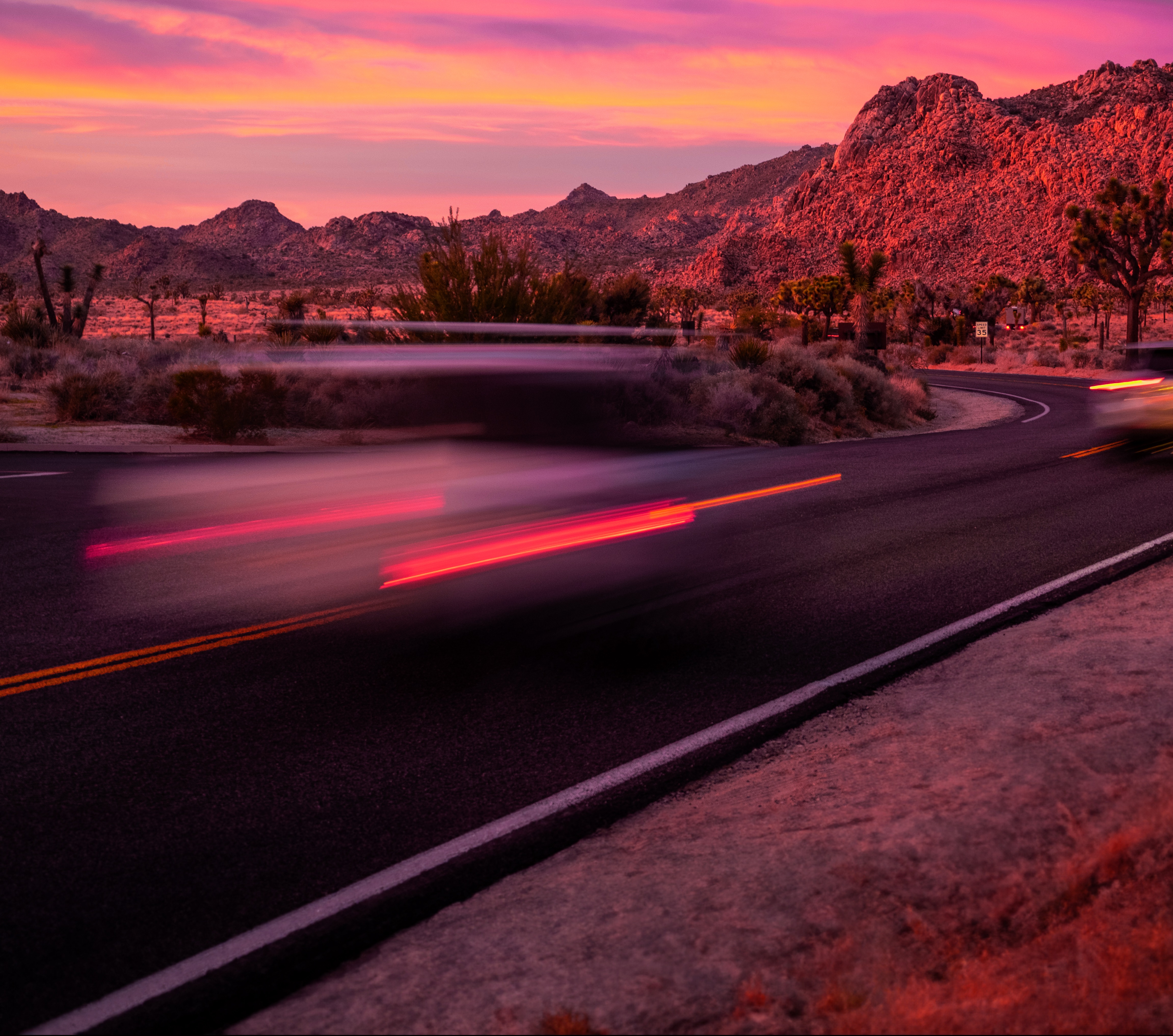 A winding road with a car traveling quickly during sunset