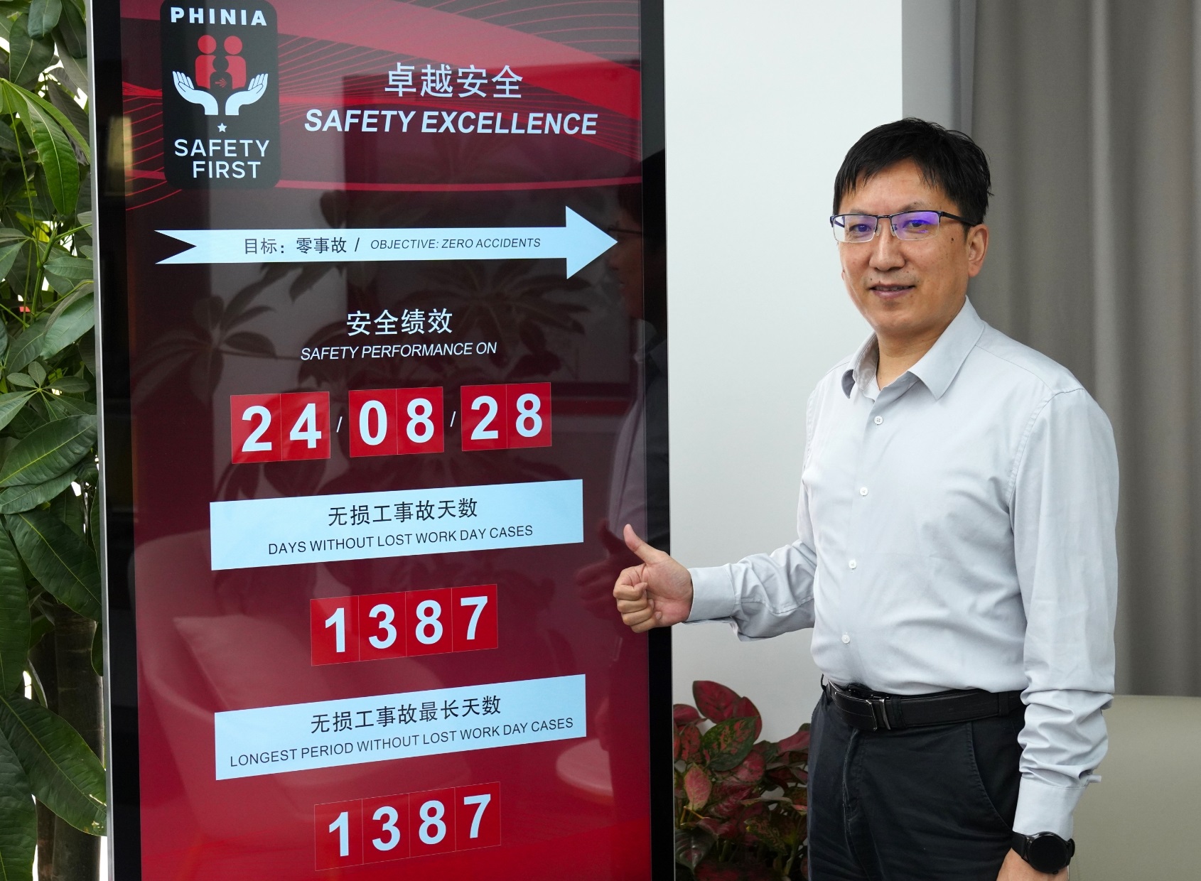 Man giving a thumbs-up next to a large digital PHINIA safety performance board displaying safety statistics