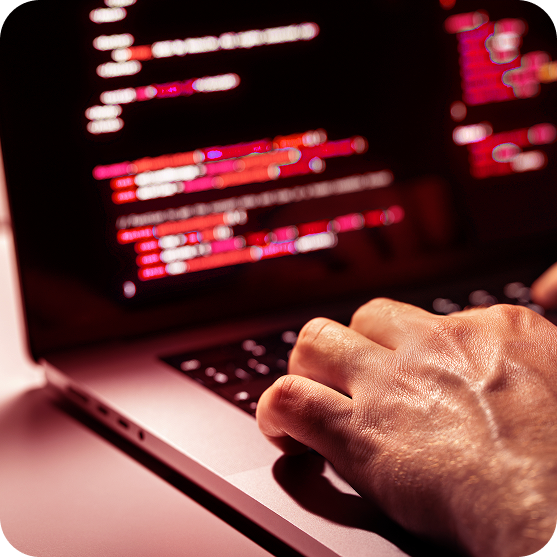 Close-up of a person working on a laptop displaying computer code related to cybersecurity.