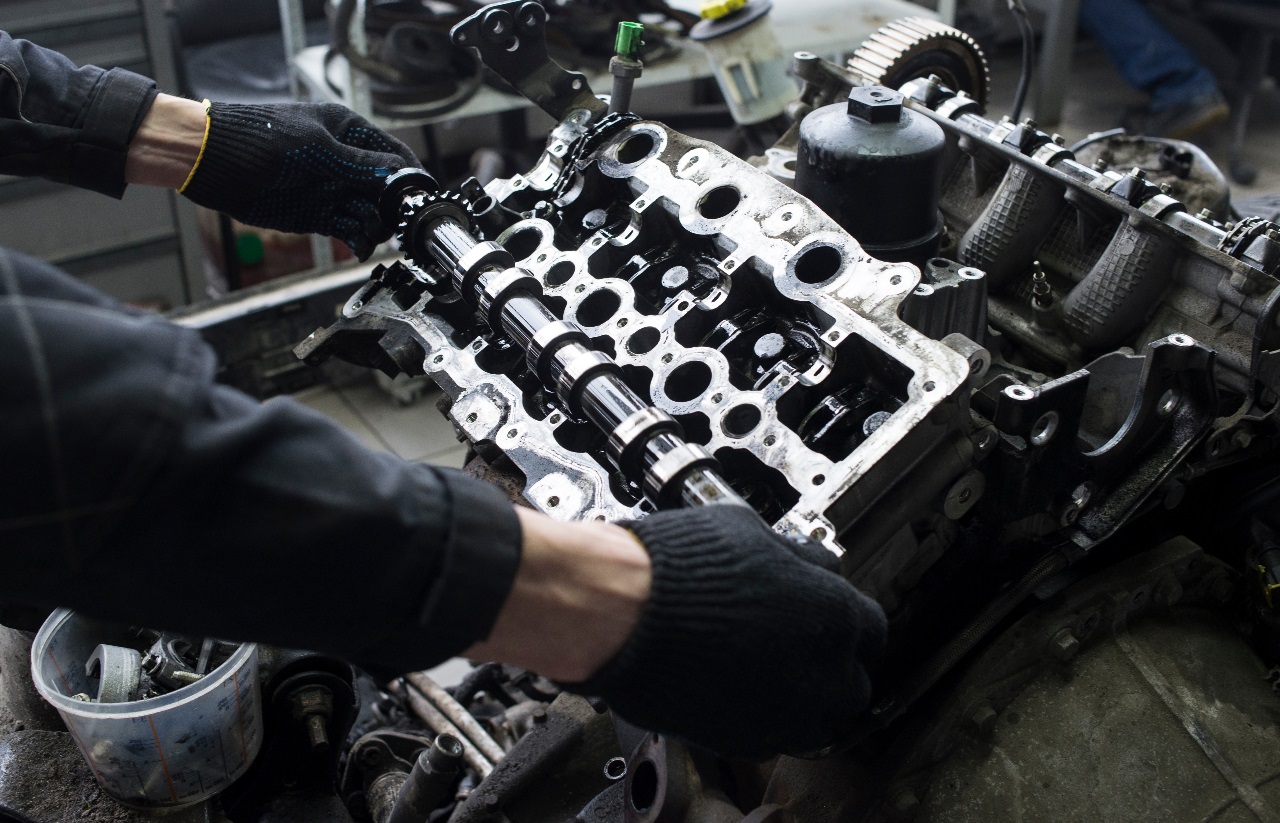 Close-up of a professional auto mechanic repairing a car engine with visible camshaft and cylinder head, showcasing high-performance engine maintenance.