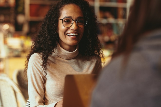 Woman with curly hair smiling in a cafe while working on a laptop