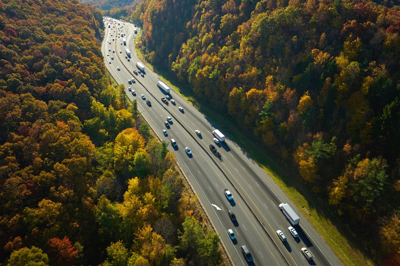 Aerial view of highway traffic cutting through a colorful autumn forest landscape, perfect for transportation, logistics, and scenic driving themes.