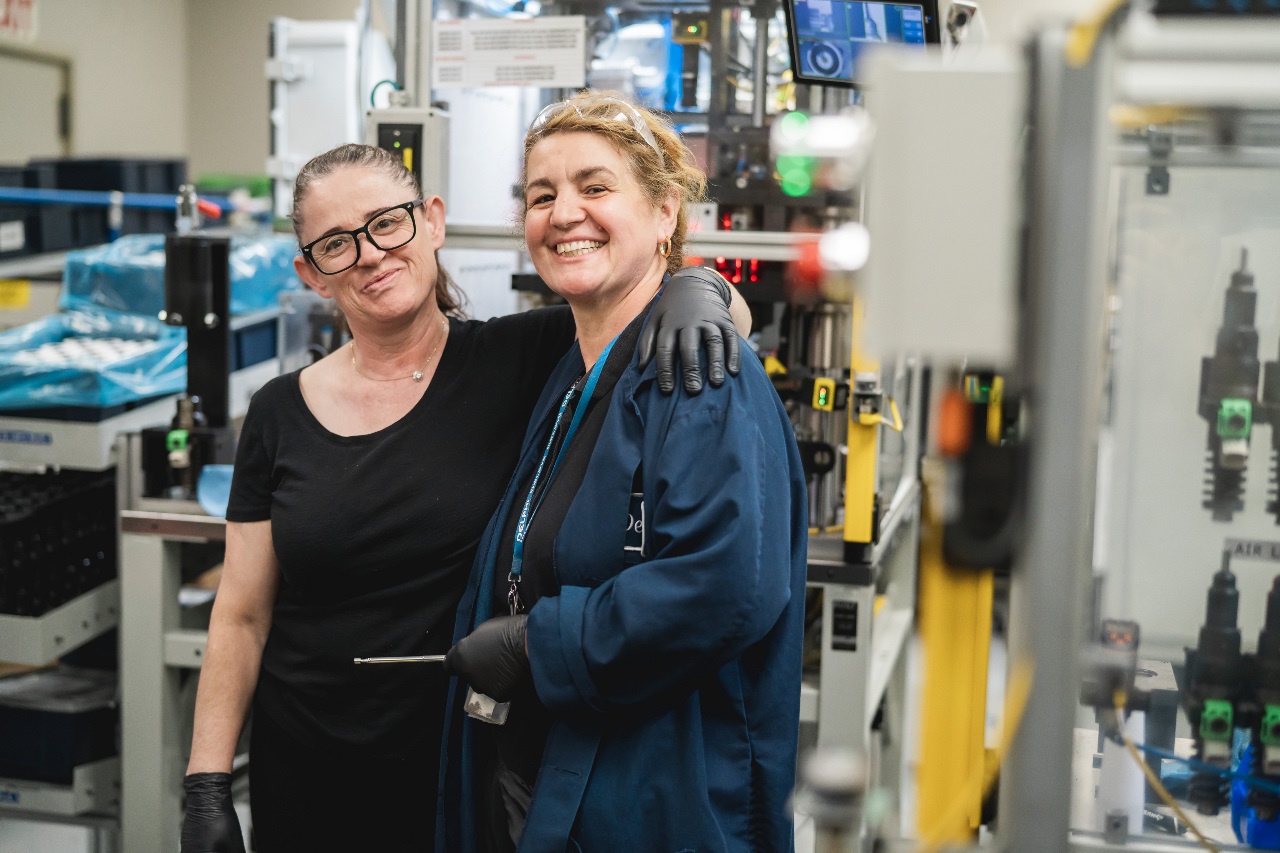 Two female workers smiling in a modern PHINIA production facility, representing workplace camaraderie and positive employee culture