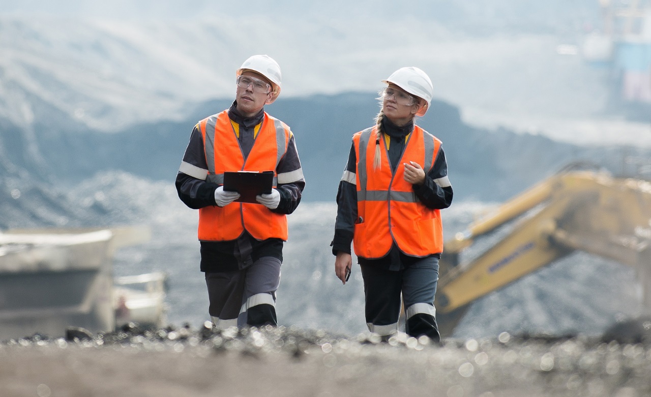 Two mining workers in high-visibility orange safety vests and helmets inspecting an open-pit mining site, symbolizing industrial safety practices.