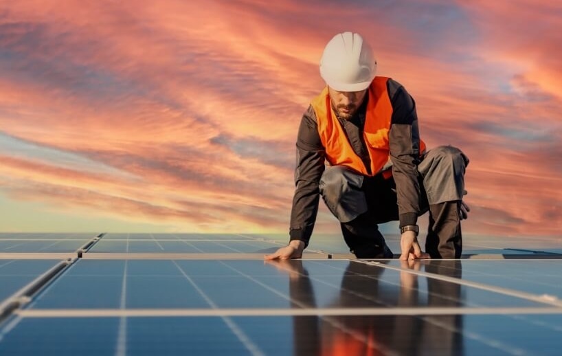 Worker fitting new solar panels to facility roof
